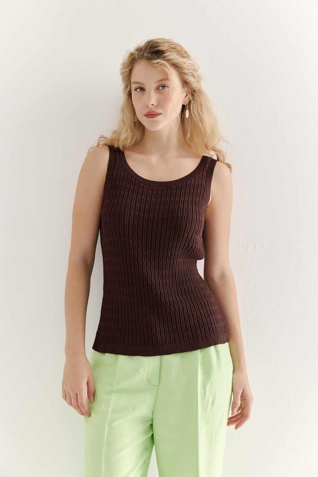 Фактурный топ-майка прилегающего силуэта из вискозной пряжи связана косами, проймы и горловина отделаны вязанными кантами. Цвет – шоколадно-коричневый.