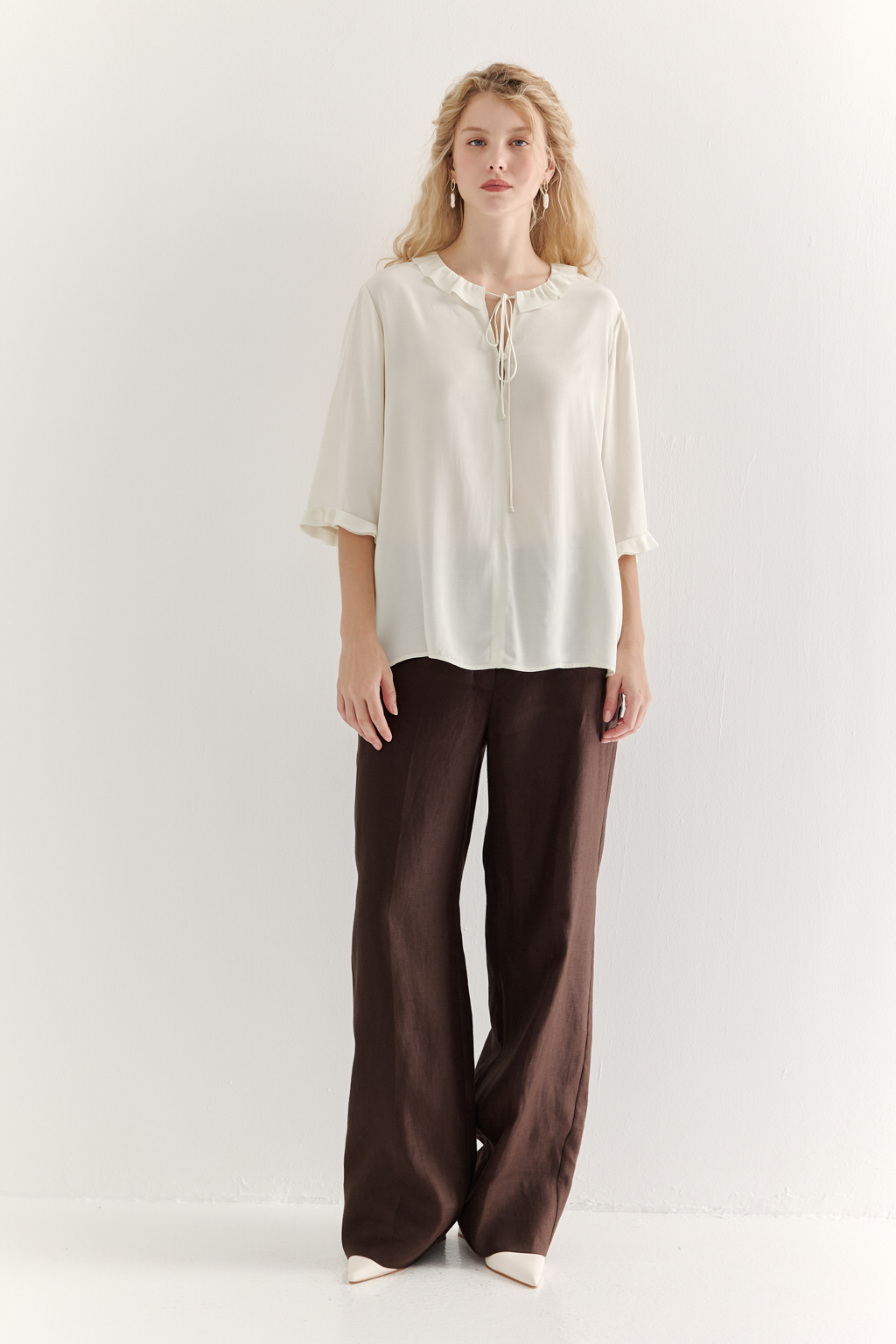 Эта романтичная блуза выполнена из вискозного крепа в нежном оттенке словочное масло. Горловина и рукава украшены изящными рюшами, добавляющими образу легкости и утонченности. Оригинальный разрез спереди кокетливо завязывается на тонкий шнур-рулик и фиксируется воздушной петлей на пуговицу. Прямой силуэт и рукава длиной одна вторая обеспечивают комфорт и свободу движений. Эта блуза — идеальный выбор для создания непринужденных, но элегантных городских образов.