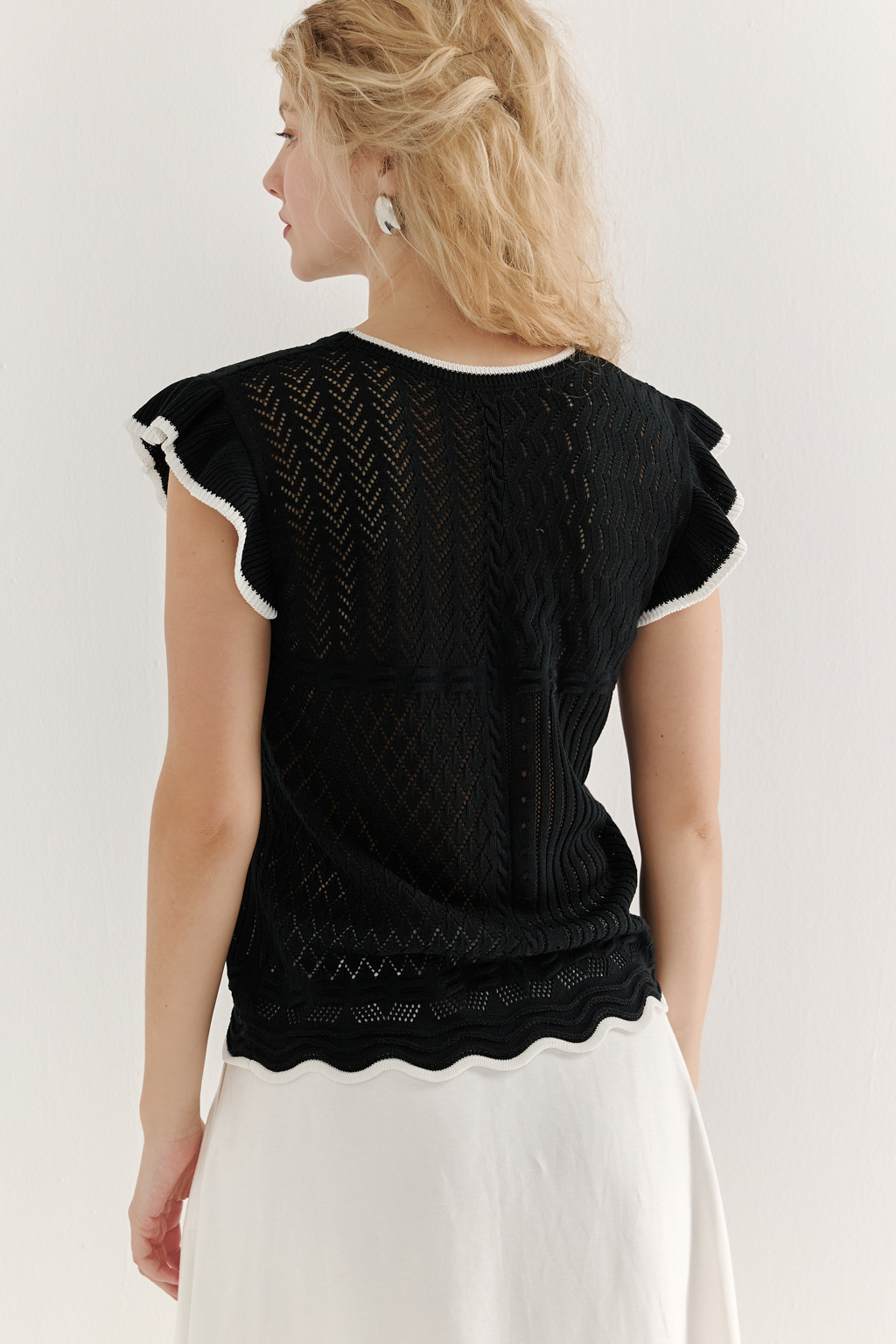 Черный топ в стиле пэчворк, в котором соединились четыре техники ажурной вязки, круглая горловина и деликатные рюши по пройме. Контрастная отделка расположена по линиям горловины, низа и краю рюши.