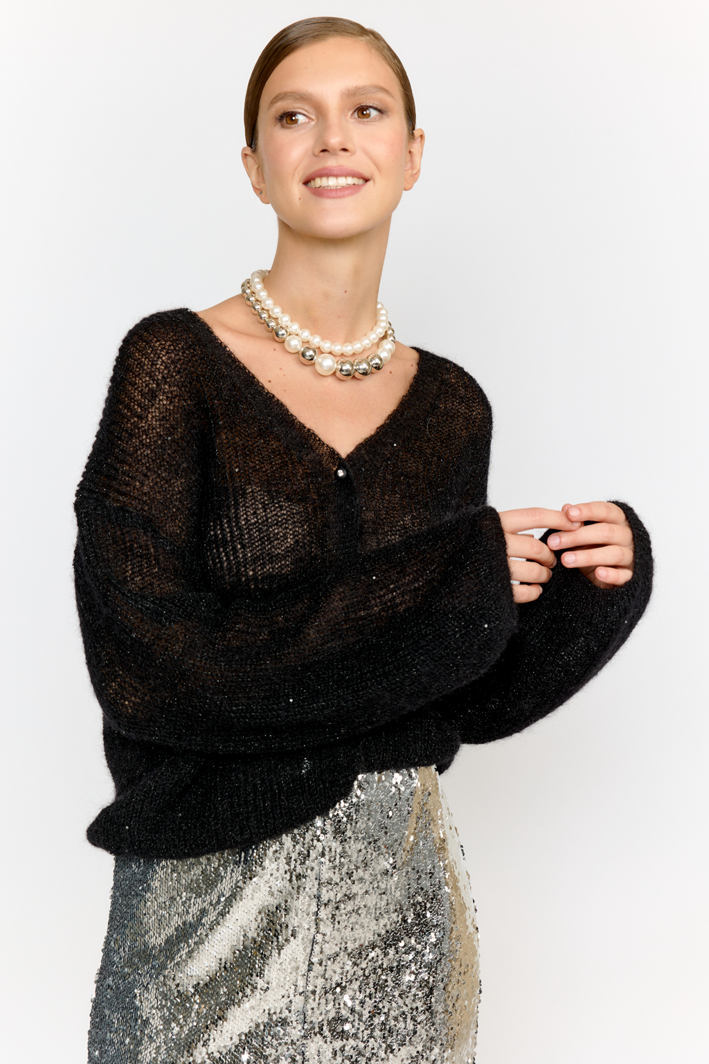 Кардиган с центральной застежкой на пуговицы, V-образной горловиной и длинным рукавом.  Модель свободного силуэта в глубоком черном  оттенке из воздушной пряжи с шерстью и мохером с деликатными мелкими пайетками, придающими легкое сияние. Кардиган очень теплый, несмотря но свою трендовую транспарентность и легкость, благодаря мохеру в составе. Шерсть так же обеспечивает естественную терморегуляцию и уют. Такой кардиган будет выигрышно смотреться в образах с  брюками и юбками из коллекции, а так же дополнит образы с платьями на бретелях или платьем-бандо.