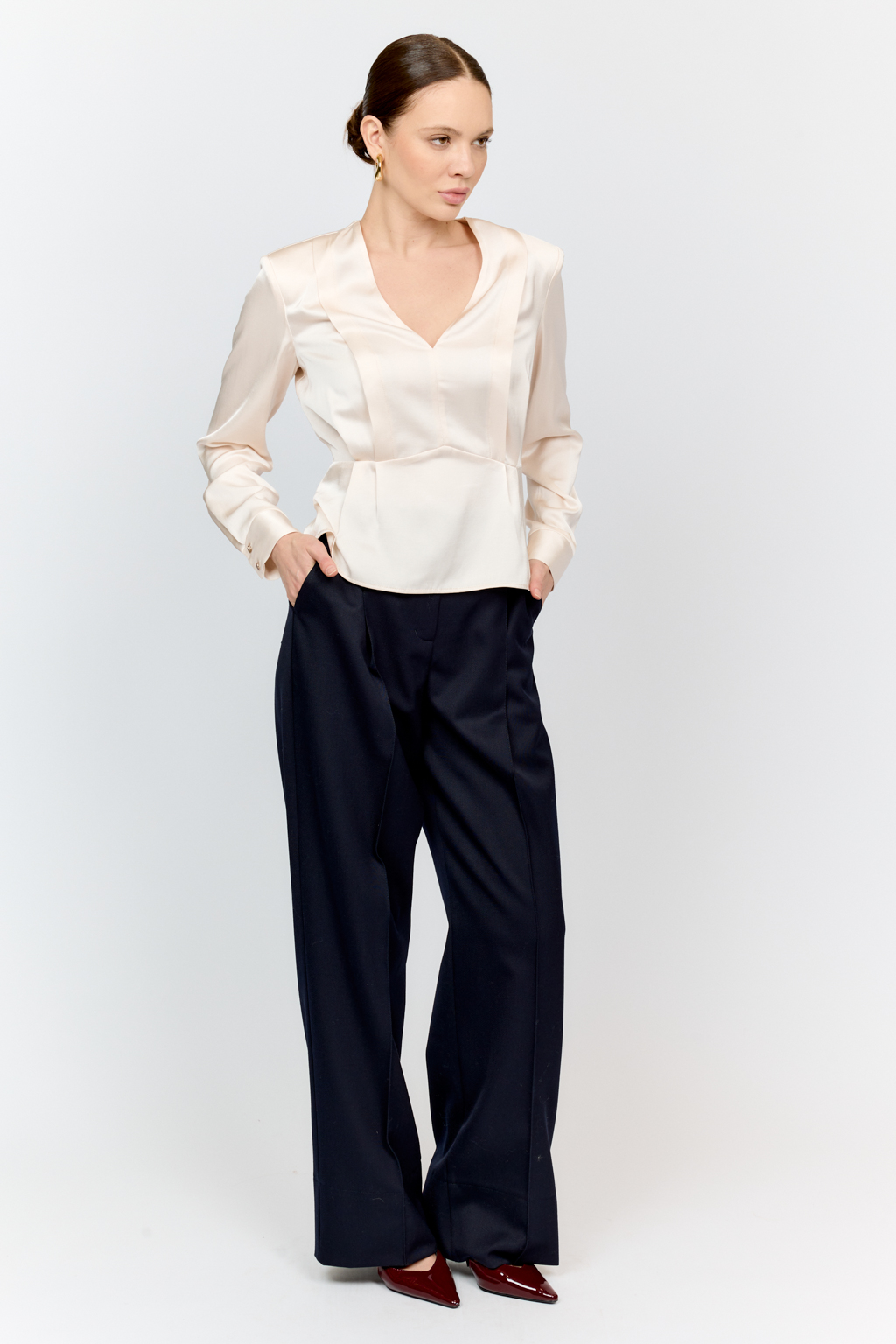 Блуза с глубоким V-образным вырезом горловины и фигурным резом по линией груди, на которой заложены глубокие складки из вискозы с атласной фактурой.