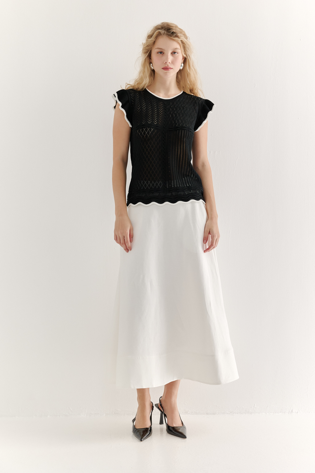 Черный топ в стиле пэчворк, в котором соединились четыре техники ажурной вязки, круглая горловина и деликатные рюши по пройме. Контрастная отделка расположена по линиям горловины, низа и краю рюши.
