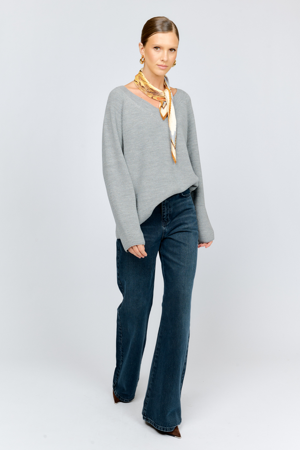 Трикотажный джемпер серого цвета свободного силуэта с V-образным вырезом горловины и рукавами реглан из шерстяной смесовой пряжи станет центром комфортных осенних образов.