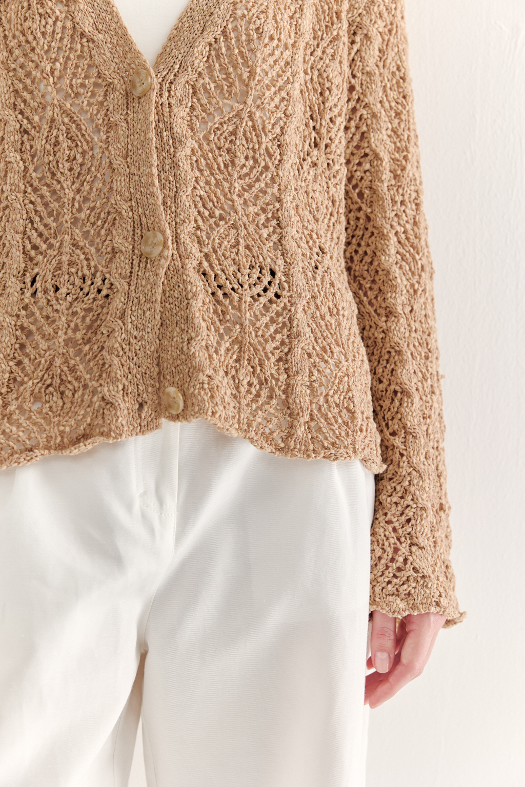 Бежевый вязаный кардиган оверсайз силуэта из хлопковой пряжи. Кардиган связан в сложной технике комбинирования сетки и ажурных ромбов. Рукав прямой удлиненный, V-образный вырез, борт отделан планкой, застежка по борту на 3 пуговицы, низ кардигана и рукав – сложные фестоны.