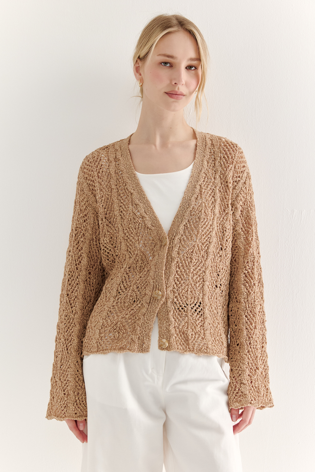 Бежевый вязаный кардиган оверсайз силуэта из хлопковой пряжи. Кардиган связан в сложной технике комбинирования сетки и ажурных ромбов. Рукав прямой удлиненный, V-образный вырез, борт отделан планкой, застежка по борту на 3 пуговицы, низ кардигана и рукав – сложные фестоны.