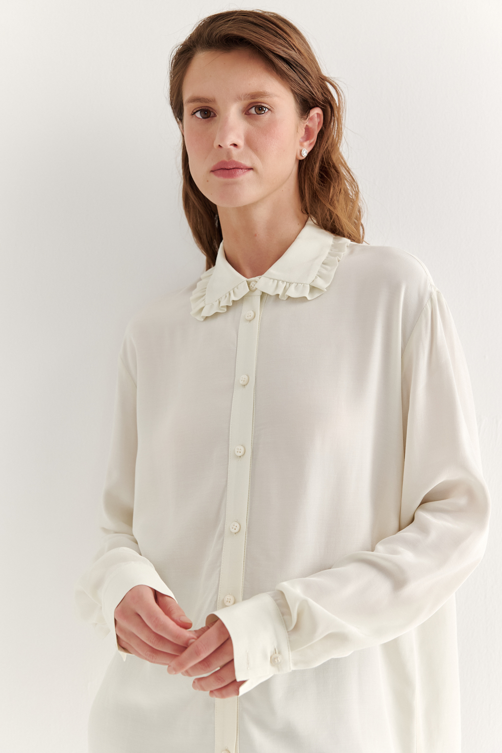 Блуза-батник в нежном оттенке сливочное масло станет изысканным дополнением к жакету, брюкам или верхней одежде, позволяя создавать актуальные многослойные образы. Изготовленная из вискозной ткани, она обладает превосходными тактильными качествами и напоминает дорогой шелковый креп. Классическая блузка свободного кроя с отложным воротником и стойкой, украшенной узким рюшем, имеет планку для застежки и втачной прямой рукав с манжетой на пуговицах.