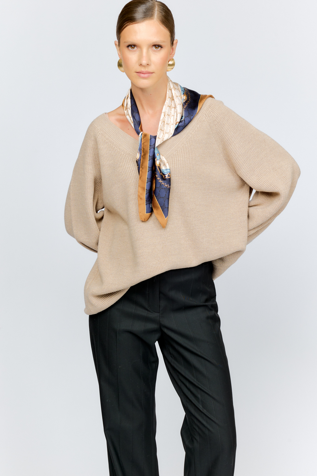 Трикотажный джемпер бежевого цвета свободного силуэта с V-образным вырезом горловины и рукавами реглан из шерстяной смесовой пряжи станет центром комфортных осенних образов.