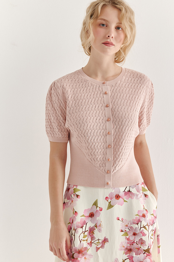 Джемпер нежно-розового цвета, связанный из тонкой тактильной пряжи, в составе которой вискоза и нейлон. В дизайне джемпера применен принцип контраста фактур, в данном случае – полупрозрачного ажура и ластика. Круглая горловина и планка с застежкой на 9 пуговиц-жемчужин, рукав длиной одна вторая.