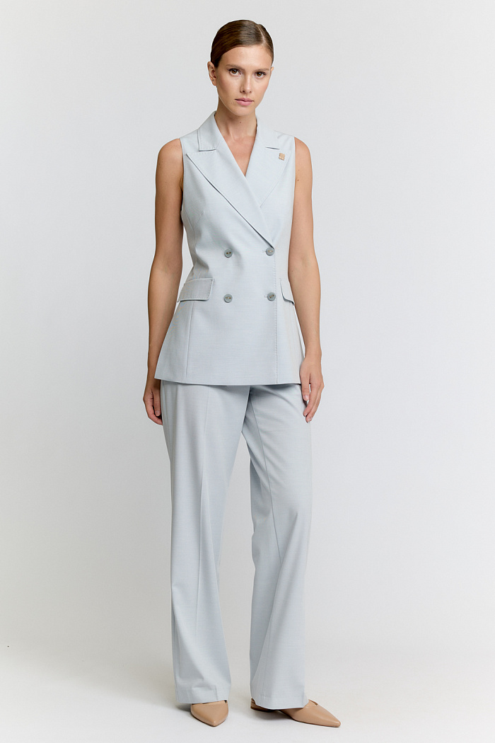 Удлинённый двубортный жилет с английским воротником отделанный ручной строчкой. По боковым швам расположены разрезы.