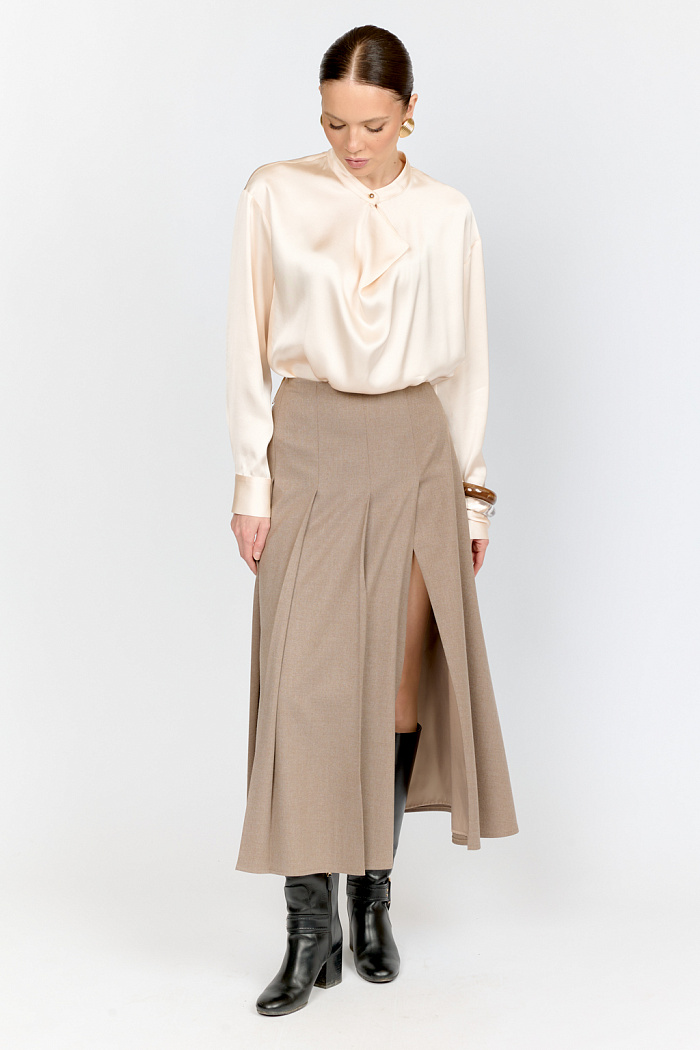 Юбка расклешенного силуэта с крупными складками и высоким разрезом спереди сбоку в длине миди выполнена из костюмной ткани песочного цвета.