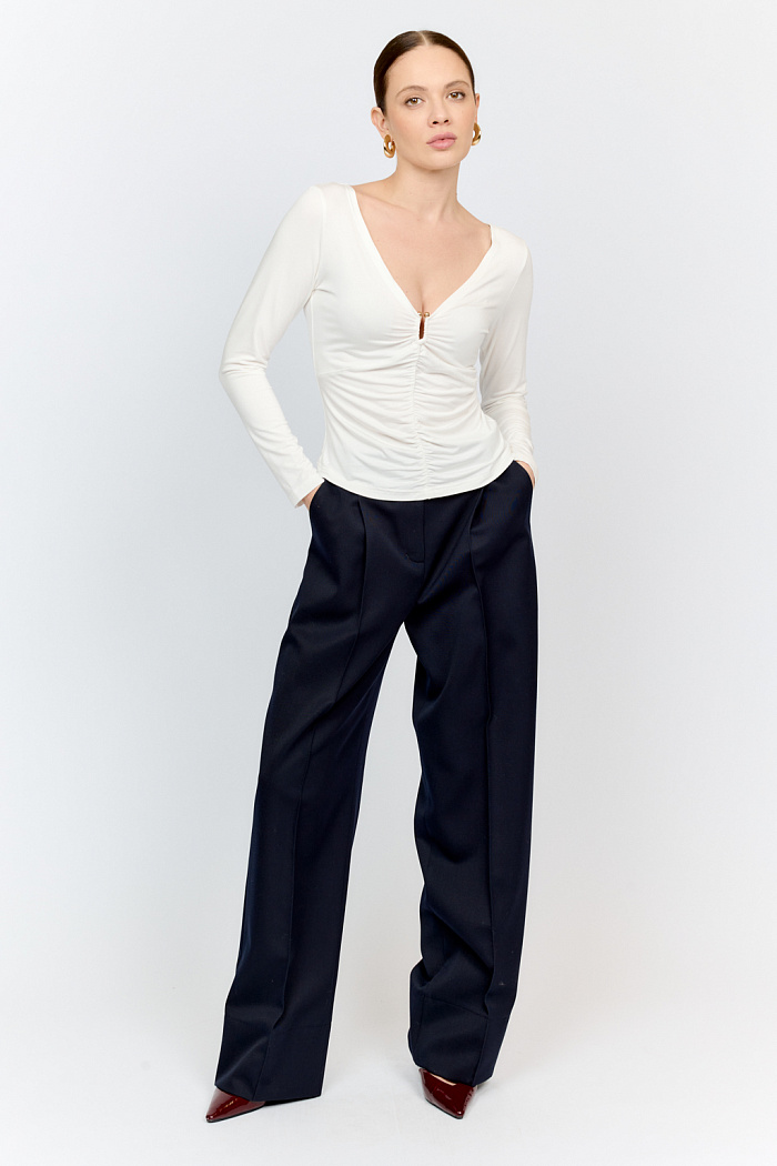 Лонгслив в цветет тофу с глубоким V-образным вырезом горловины и декором из металла в золотом оттенке. Спереди ткань драпируется в области груди и по средней линии полочки. Изделие подарит приятные тактильные ощущения в носке. Подойдет для стилизации со множеством образов.