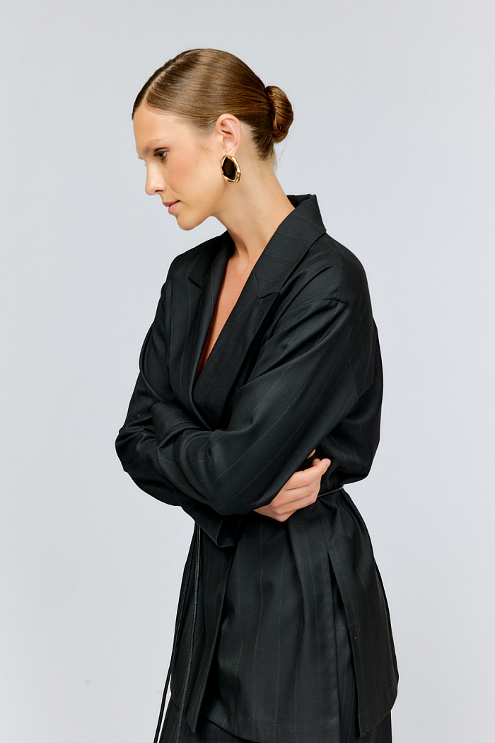 Жакет прямого кроя из костюмной ткани в деликатную трендовую полоску с манжетами на рукавах и разрезами по бокам комплектуется поясом-шнурком на талию.