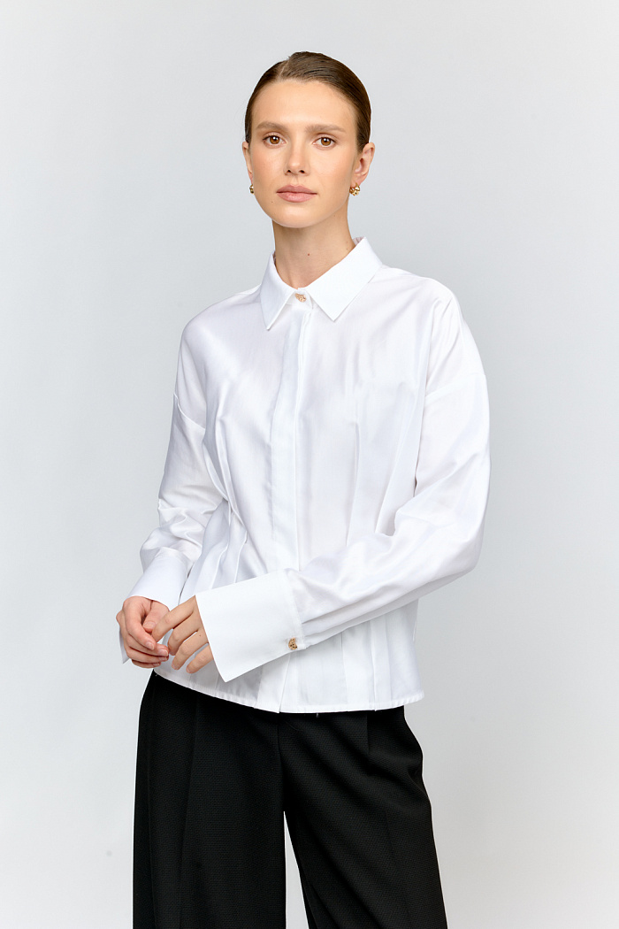 Укороченная рубашка со спущенными плечами изткани белого цвета с жемчужным переливом  — стильная вещь для создания  разных образов. Складки по полочке структурируют силуэт, выгодно подчеркивая талию, а спущенное плечо создаёт современный силуэт. Сочетайте с джинсами и брюками, юбками различных фасонов, лоферами или балетками, сумкой через плечо.