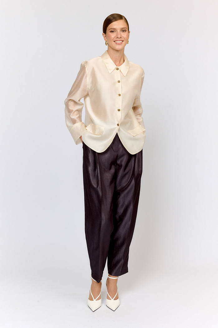 Блуза-жакет среднего объёма с отложным воротником и застежкой на пуговицы. Спереди декоративные клапаны, имитирующими карманы жакета. Спереди изделие двухслойное, сзади - в один слой ткани с легкой прозрачностью.  Выполнена из легкой полупрозрачной ткани из тенселя  с содержанием шёлка. Тенсель  -  волокно растительного происхождения, получаемое из древесины эвкалипта по экологически чистому технологическому процессу. Отличается  воздухопроницаемостью и гигроскопичностью.  Шёлк обеспечивает роскошный внешний вид и пластичность ткани.  Преимущества ткани: шелковистая поверхность ткани с жемчужным переливом выглядит премиально и нарядно. Легкая прозрачность делает образ трендовым.  Необычное решение облегченного жакета  в  нежном цвете "шампань" поможет создать уникальный модный образ для праздничного вечера.